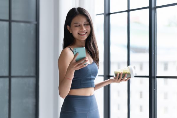 Woman smiling while checking smartphone and holding drink by window