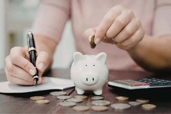 Person putting coin into piggy bank beside pen and calculator